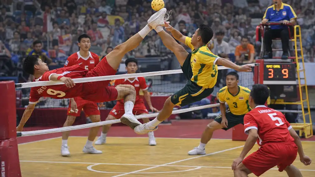 Match de sepak takraw : joueur en smash acrobatique au-dessus du filet avec balle rotin, action en salle.